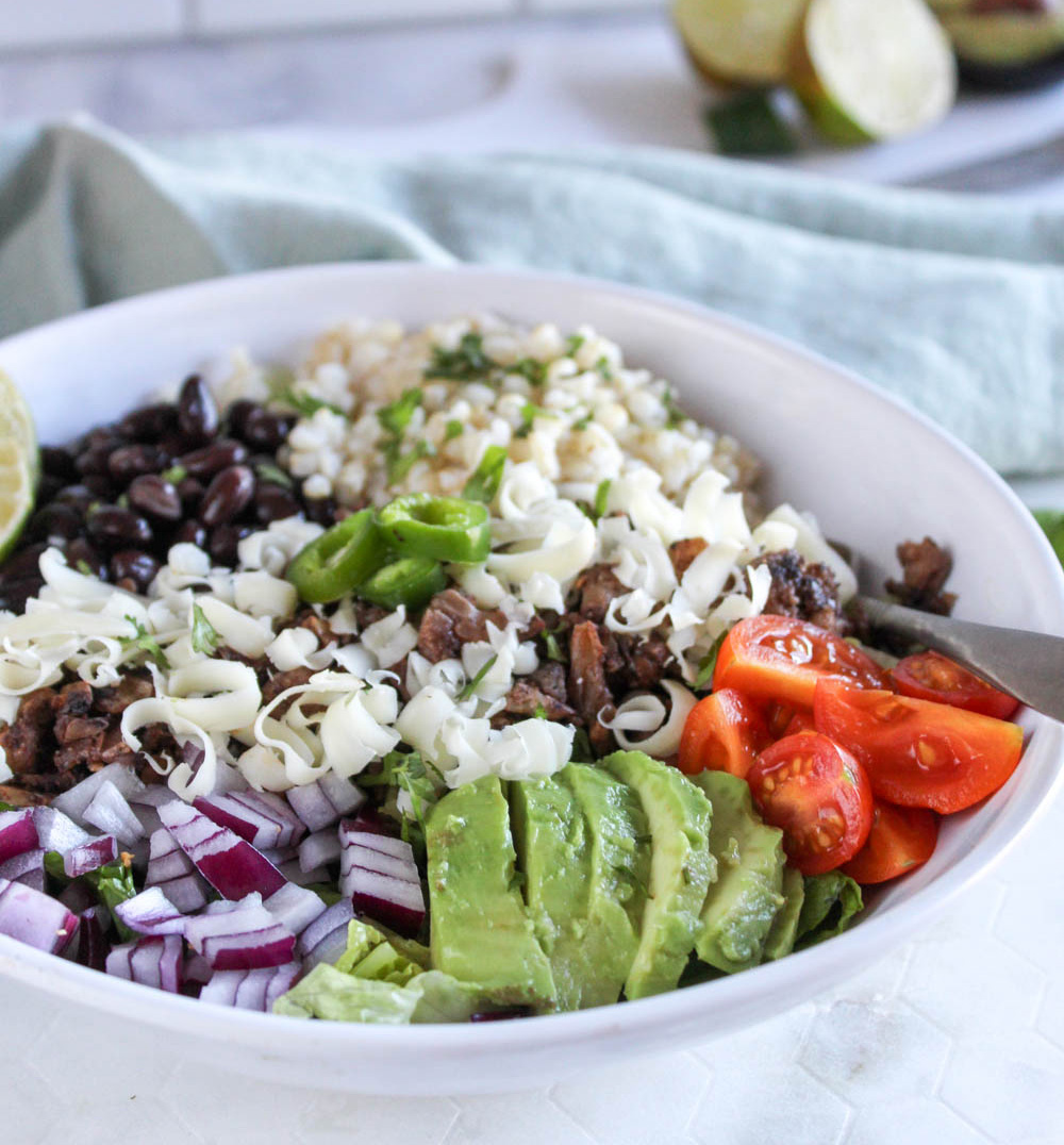 close up picture of vegetable burrito bowl with avocados, onions and jalapeno peppers on top