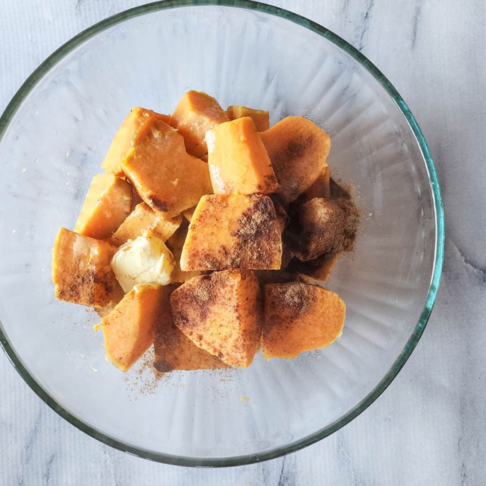 cooked sweet potato wedges in a glass mixing bowl with seasoning on top