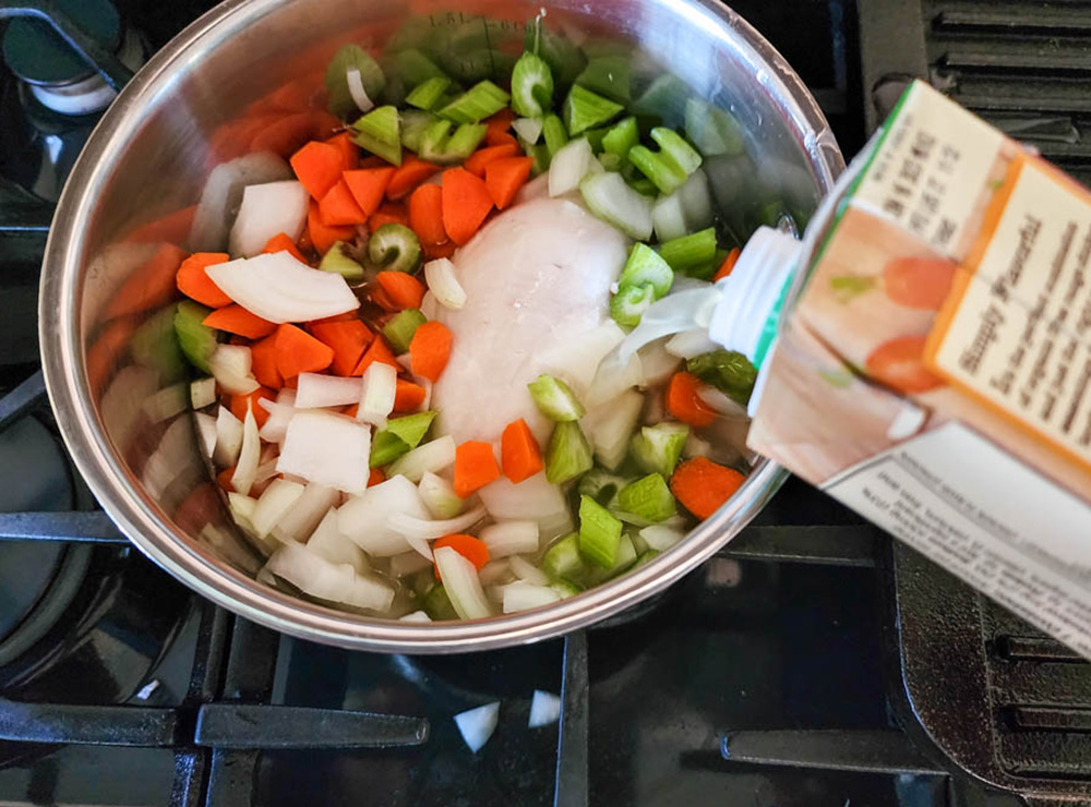 a picture of vegetables and chicken in a pot with broth pouring in