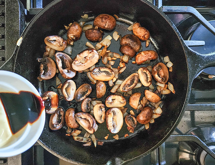 mushrooms cooking in a skillet with balsamic vinegar being added