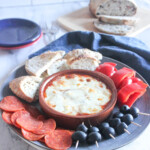 Pizza dip with melted mozzarella cheese in a bowl with bread, pepperoni, olives and peppers