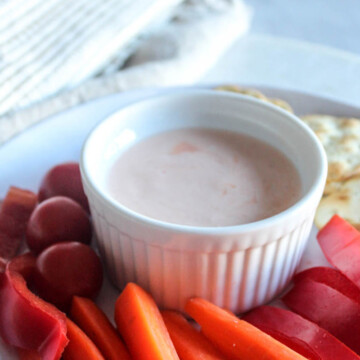 A close up picture of sriracha dipping sauce on a plate with carrots peppers and crackers