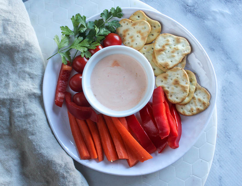 overhead view of sriracha dipping sauce with carrots peppers and crackers on a plate