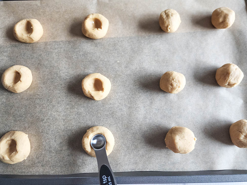 butter cookie dough on baking sheet with spoon inserted to make a well