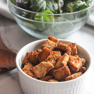 Croutons in a white bowl with a bowl of salad in the bacground
