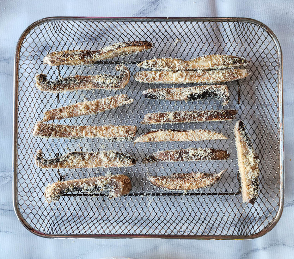 mushroom fries on an air fryer basket breaded and ready to be cooked