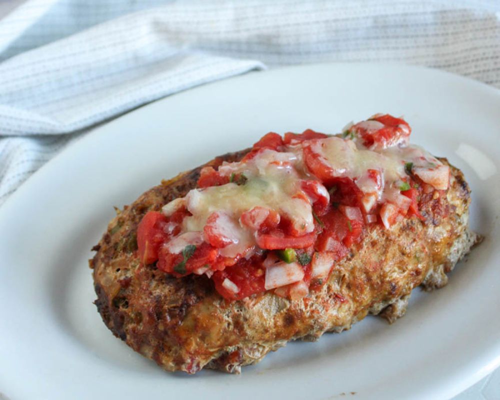 slow cooker turkey meatloaf step 4, cooked meatloaf covered with tomatoes and cheese on a platter