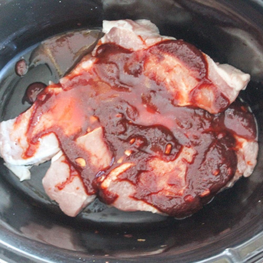 Honey garlic pork chops process step 2 . Four Pork chops ina slow cooker with sauce on top.