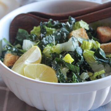 close up of kale salad in a white bowl with two spoons