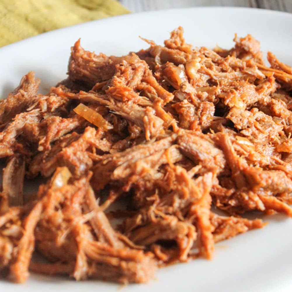 shredded bbq pulled pork covered in homemade bbq sauce on a white platter