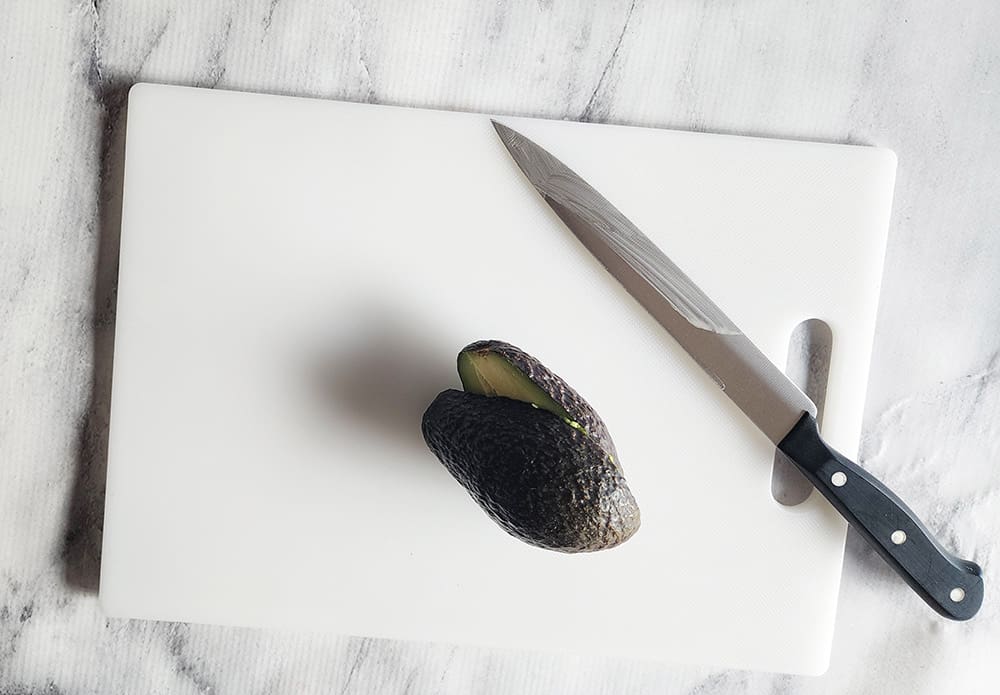 An avocado on a cutting board cut in half separated