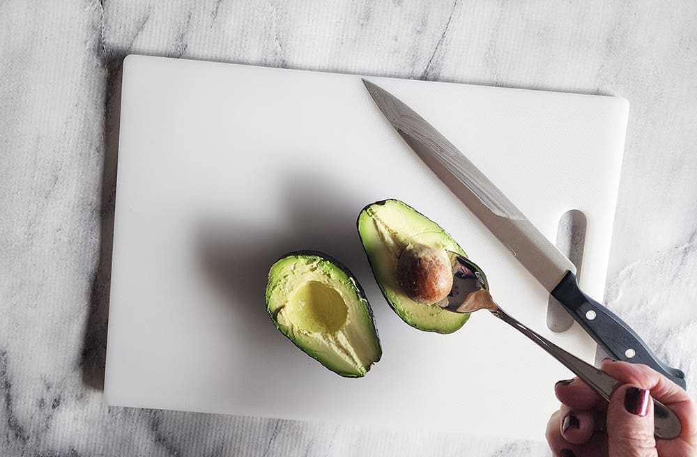 an avocado on a cutting board with pit being scooped out