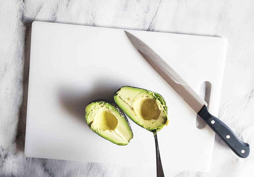 a picture of an avocado cut in half with a spoon scooping flesh out