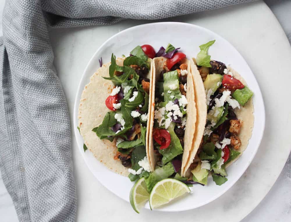 An overhead view of 3 tacos on a plate with lime slices