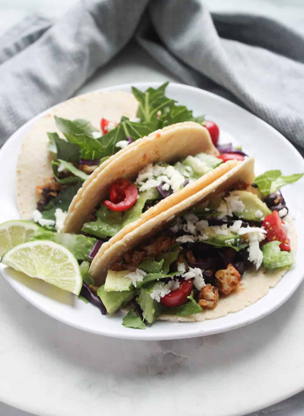 a picture of three cauliflower tacos on a plate with lettuce and limes