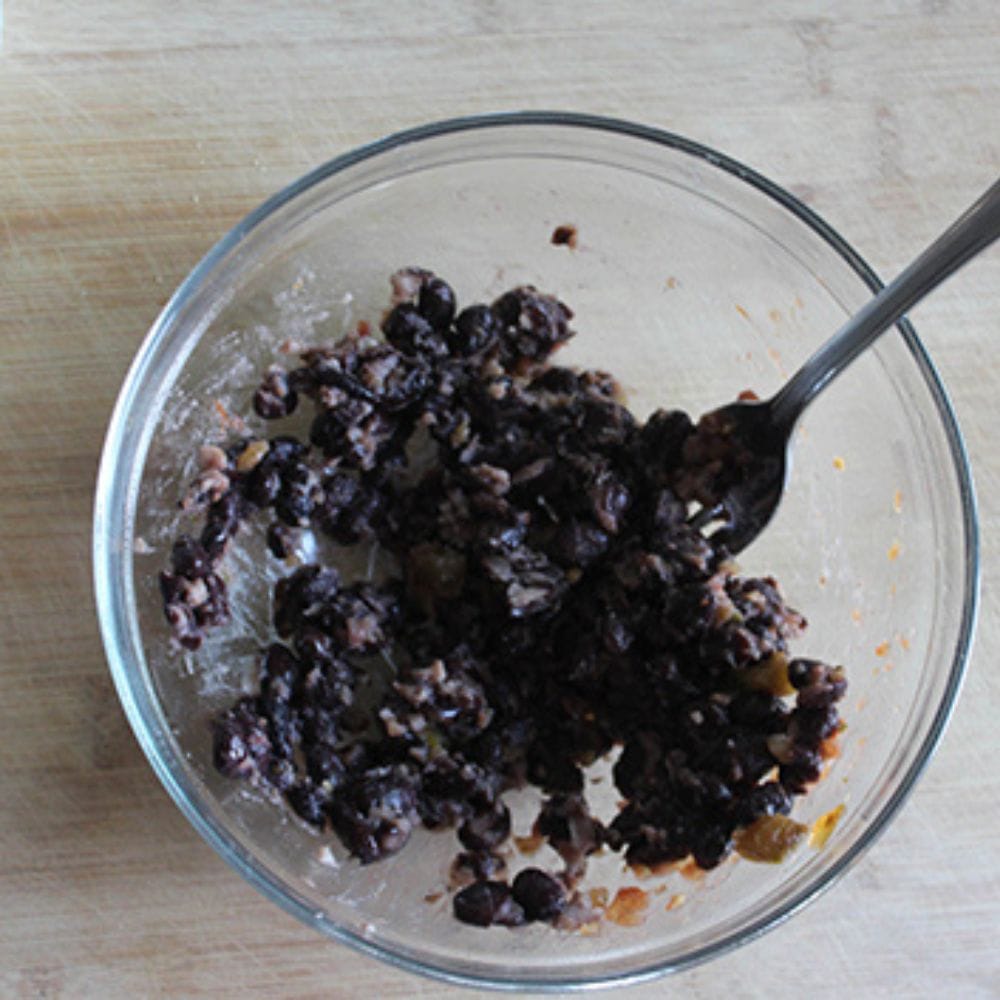 a picture of black beans smashed in a bowl with a fork