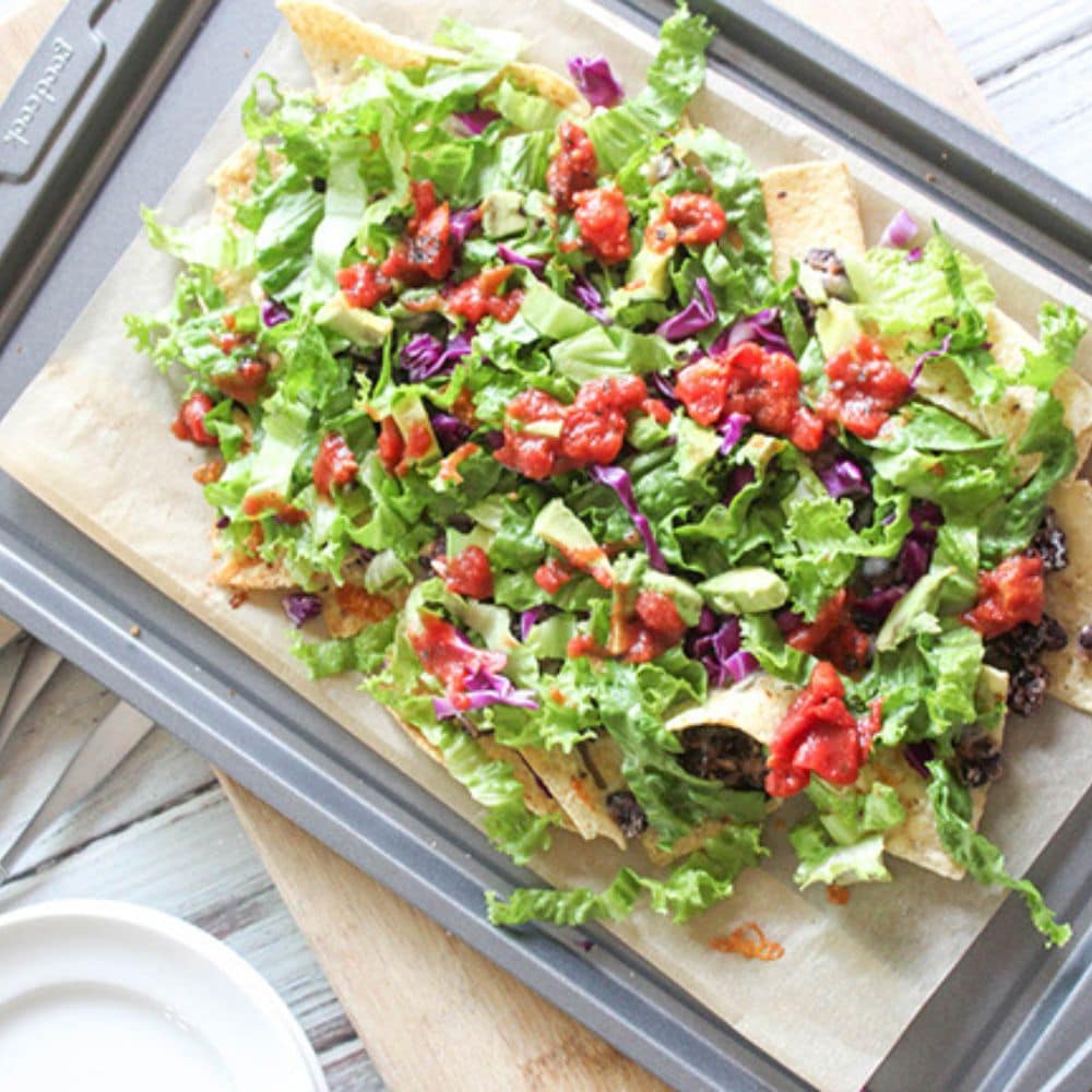 sheet pan nachos on a baking sheet topped with lettuce and salsa