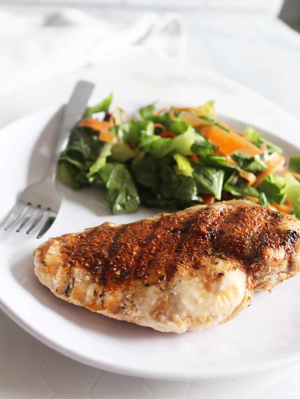 a cooked chicken breast covered in blackened seasoning on a plate with a salad