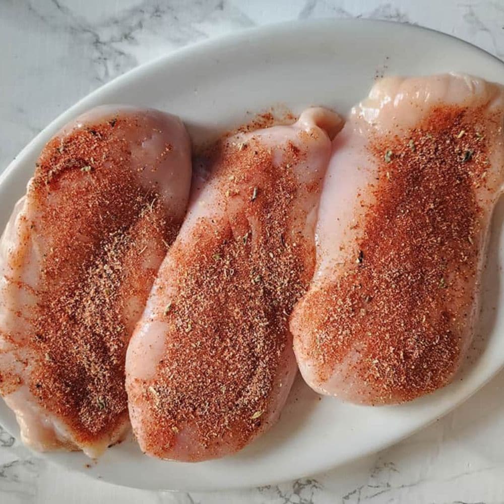 two boneless chicken breasts covered in chili powder and cumin on a plate