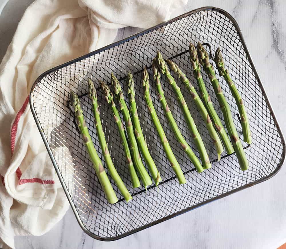 a picture of raw asparagus in an air fryer tray not cooked