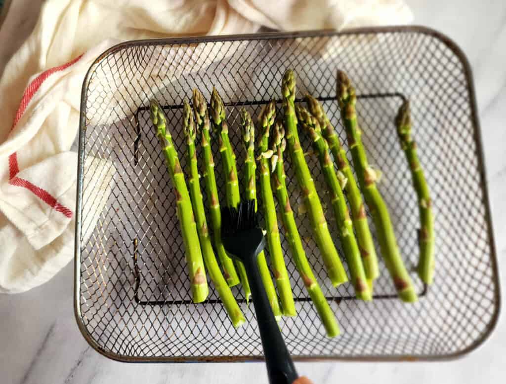 a picture or pastry brush adding butter to asparagus