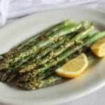 a picture of air fried asparagus on a white plate with lemon slices