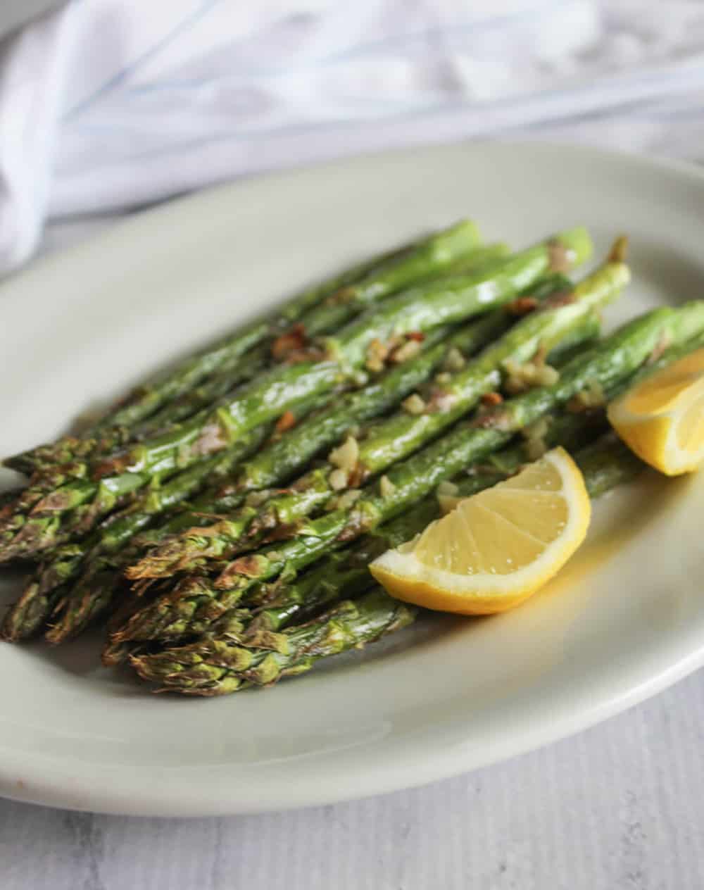 a picture of air fried asparagus on a white plate with lemon slices