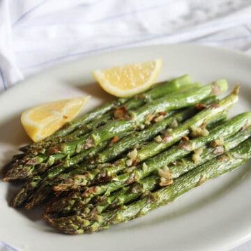 a picture of air fried asparagus on a white plate with lemons