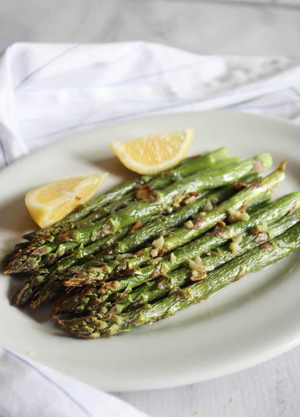 a picture of air fried asparagus on a white plate with lemons