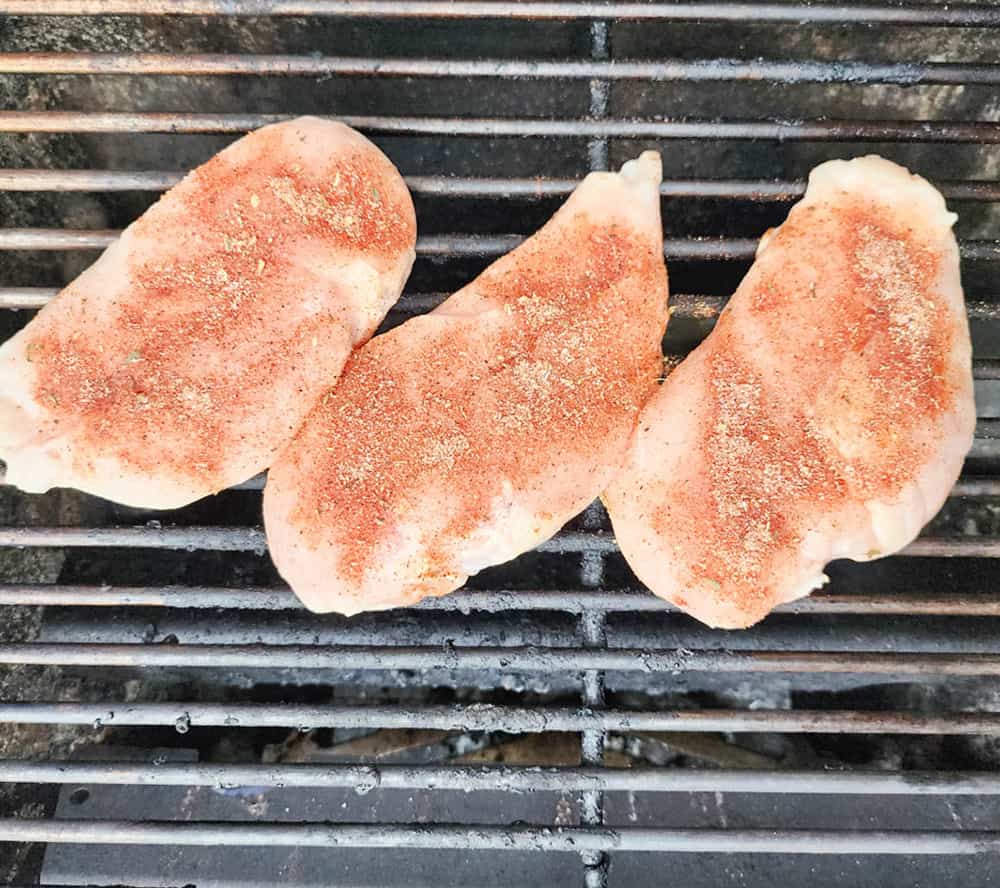 3 chicken breasts covered in blackened seasoning on the grilll