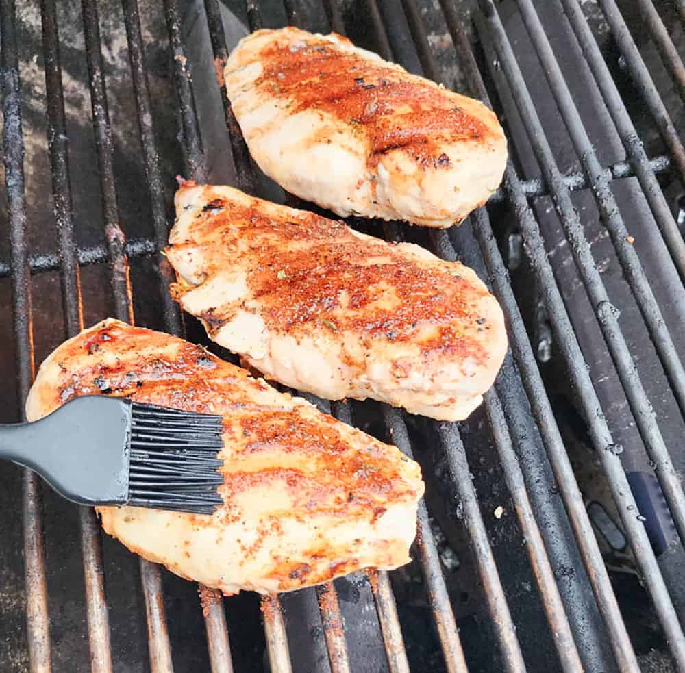 a brush brushing oil onto chicken breast on the grill