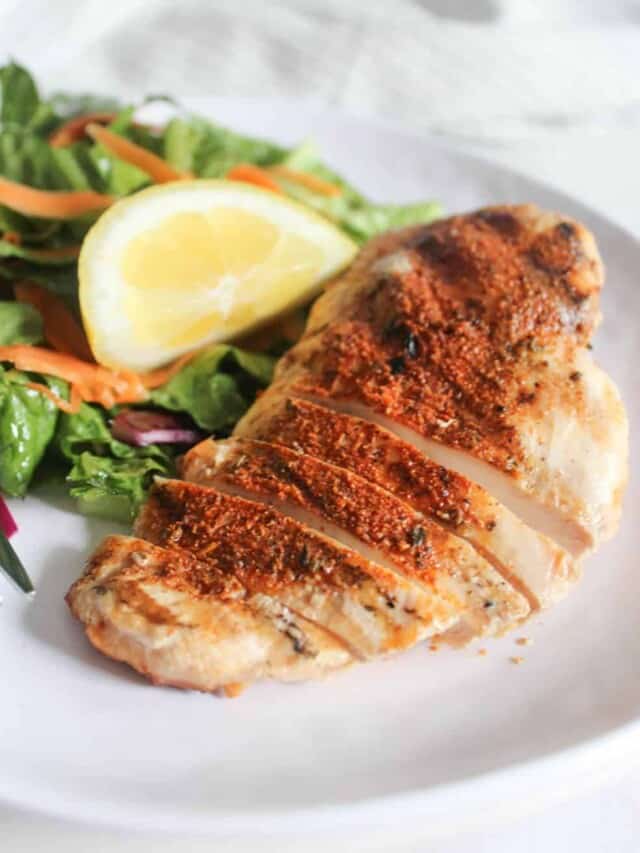 a picture of blackened chicken sliced on a plate with a salad and a wedge of lemon