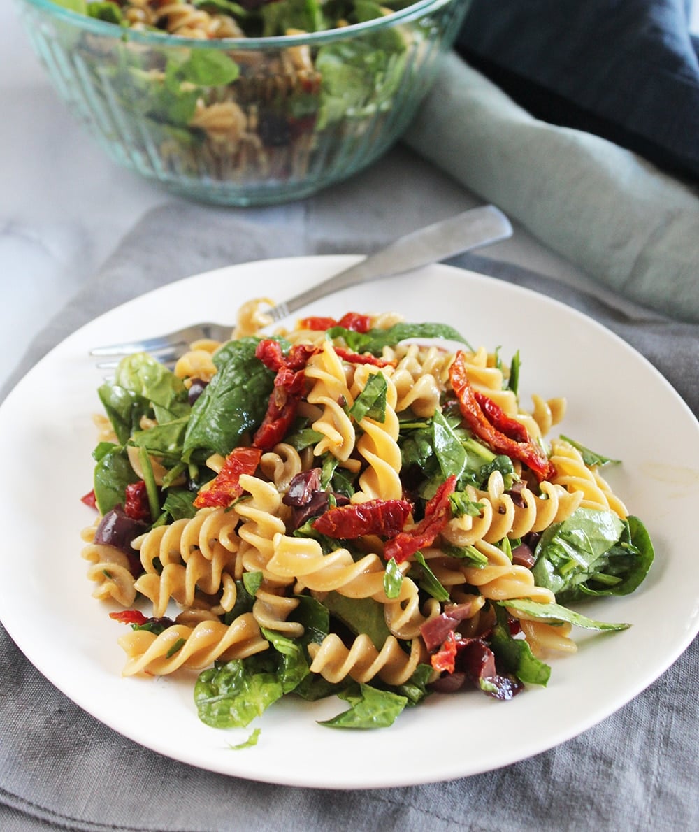 A picture of pasta salad on a plate with a fork with a bowl of salad in the background