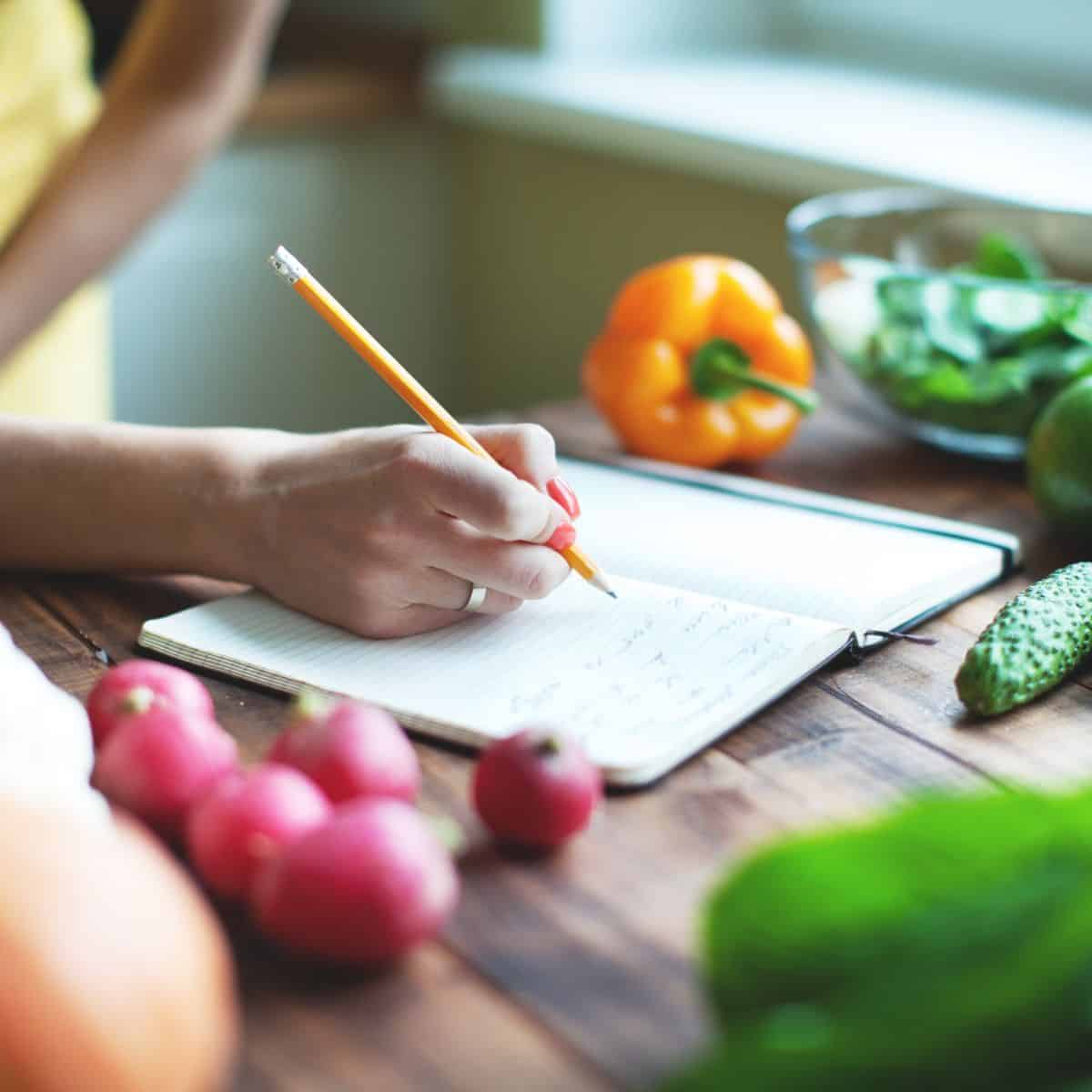 a picture of hand writing on a tablet with vegetables around it