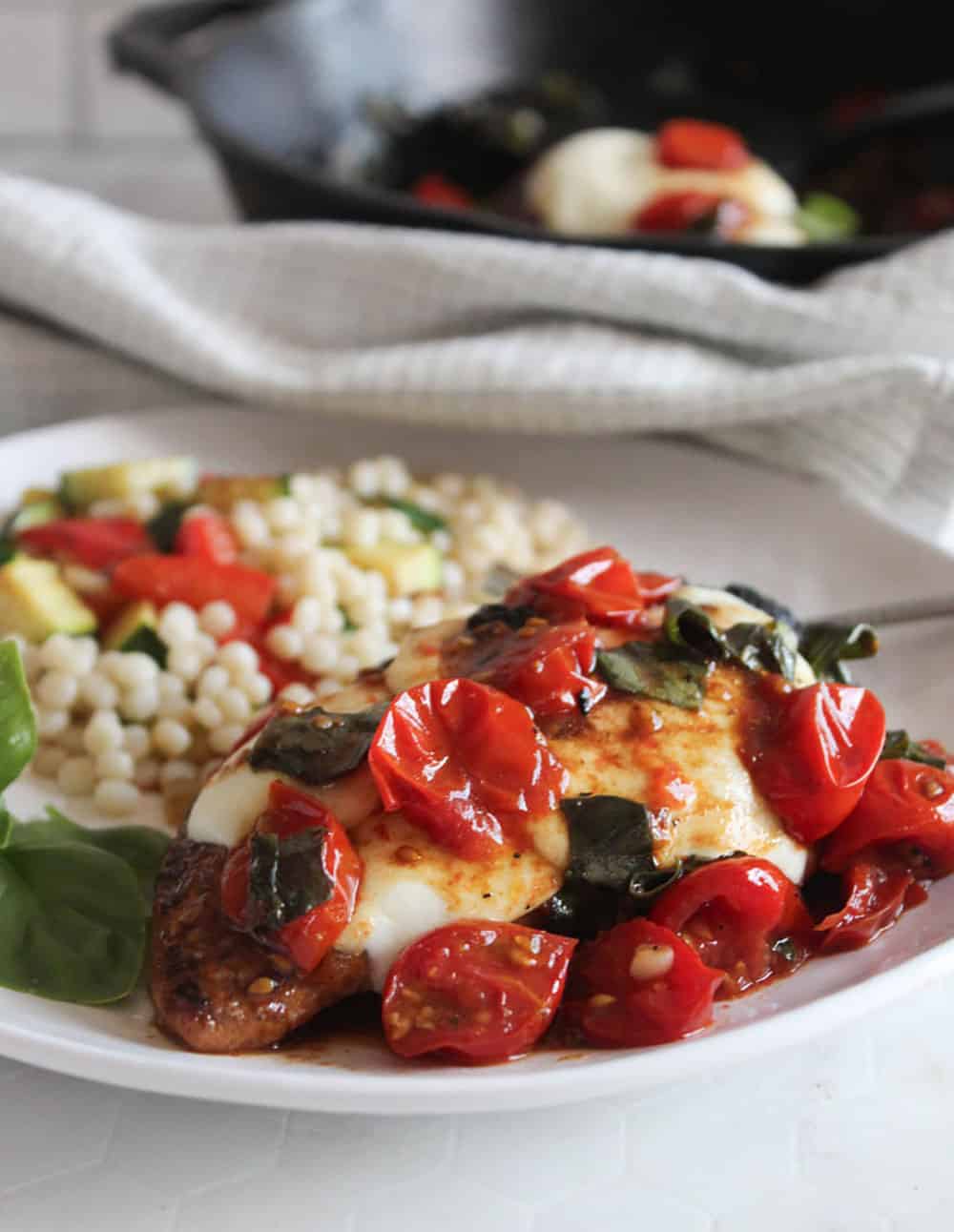 a close up of chicken caprese on a white plate with fresh basil and pasta side dish