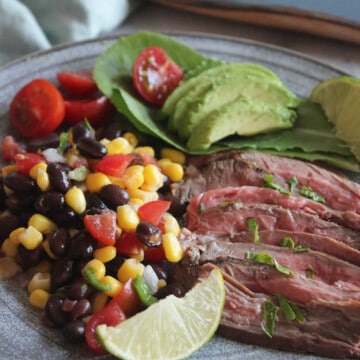 A picture of sliced flank steak, corn and limes on a plate