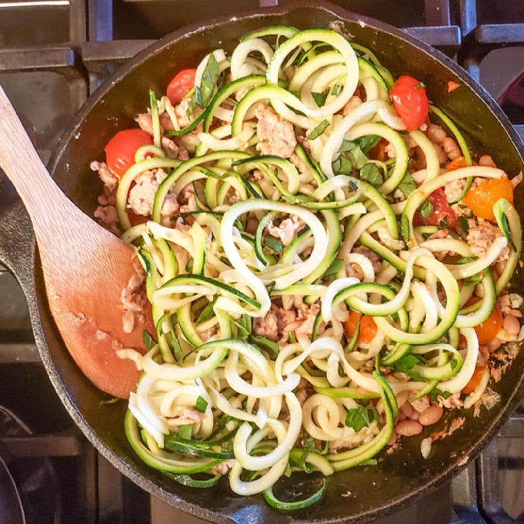 the zucchini noodles are added to the skillet, with chicken and tomatoes