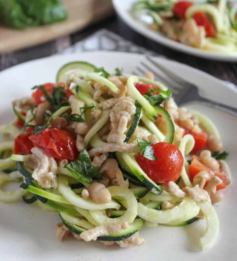 This image is plated zucchini noodles recipe with chicken and tomatoes. The serving is on a white plate with a fork to the side.