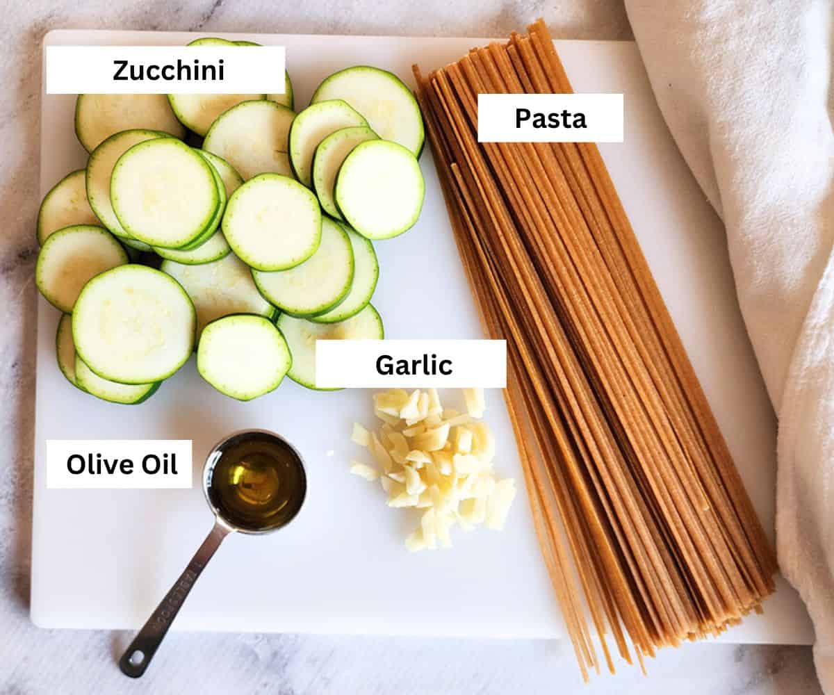 overhead view of ingredients to make zucchini pasta with sliced zucchini, olive oil, garlic, pasta