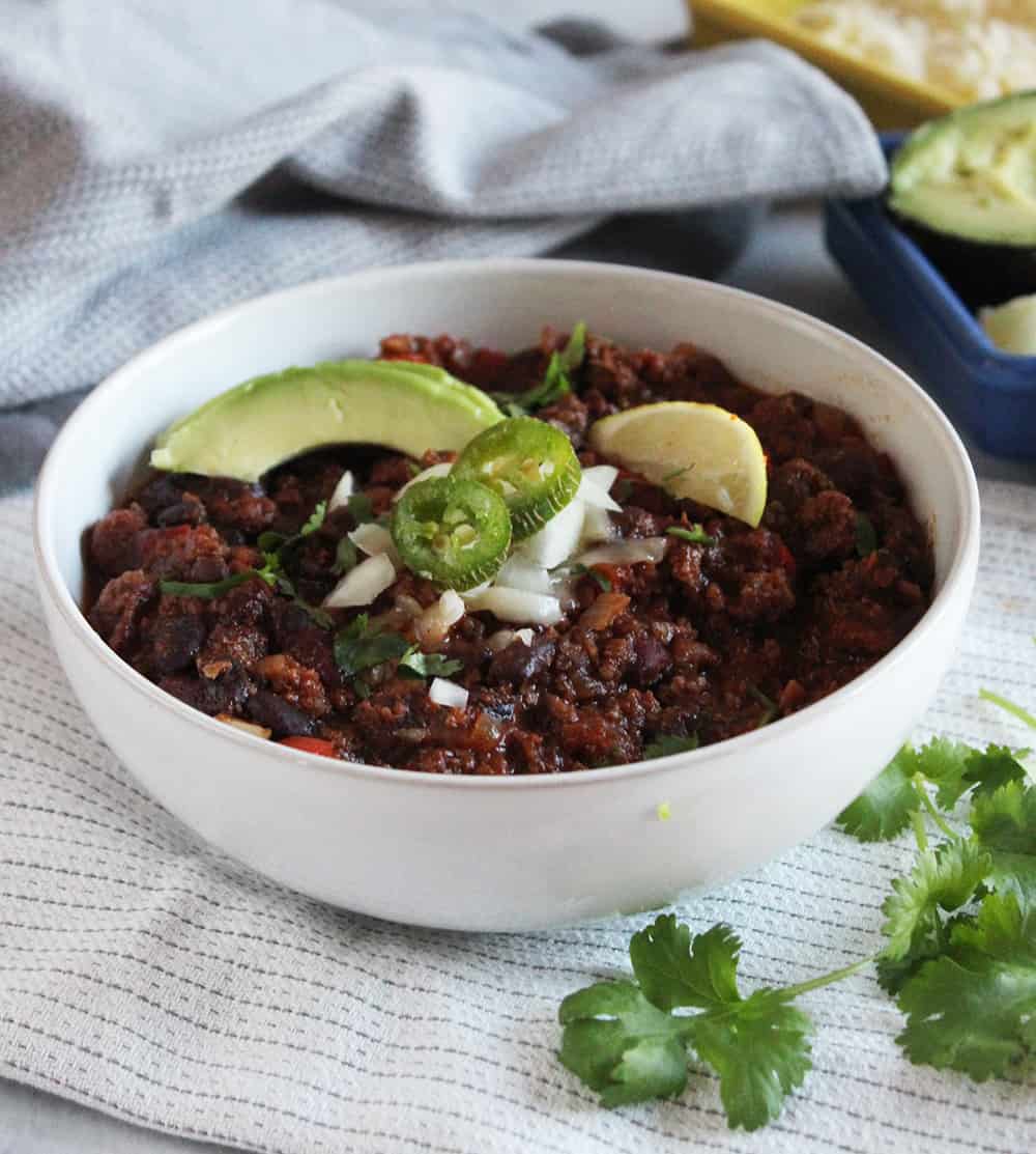 A picture of bison chili in a bowl with slices of avocado and lime on top