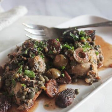 a picture of chicken marbella on a platter with sauce and a serving fork
