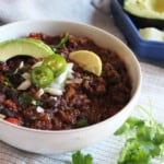 A picture of bison chili in a bowl with slices of lime, jalapenos and avocados