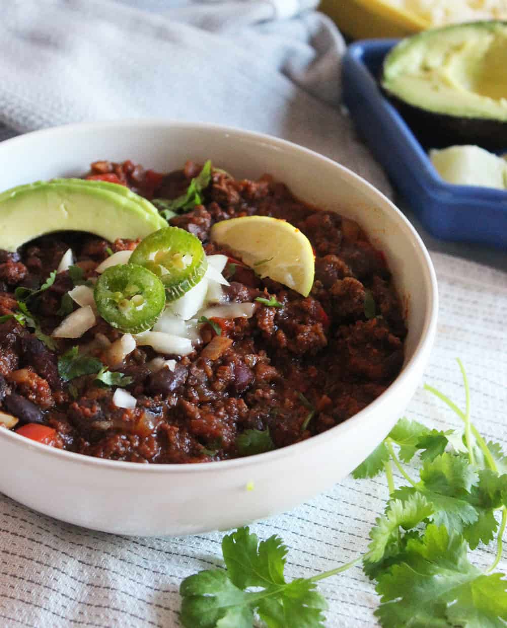 A picture of bison chili in a bowl with slices of lime, jalapenos and avocados
