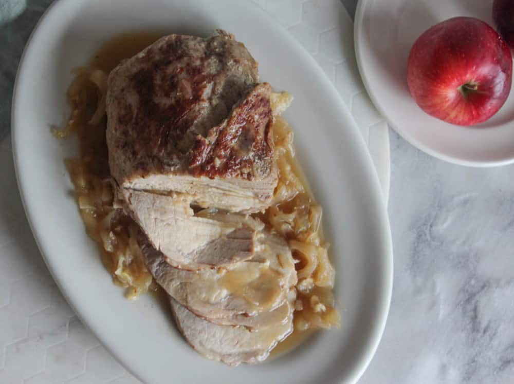an overhead view of pork roast on a white plate with gravy and onions