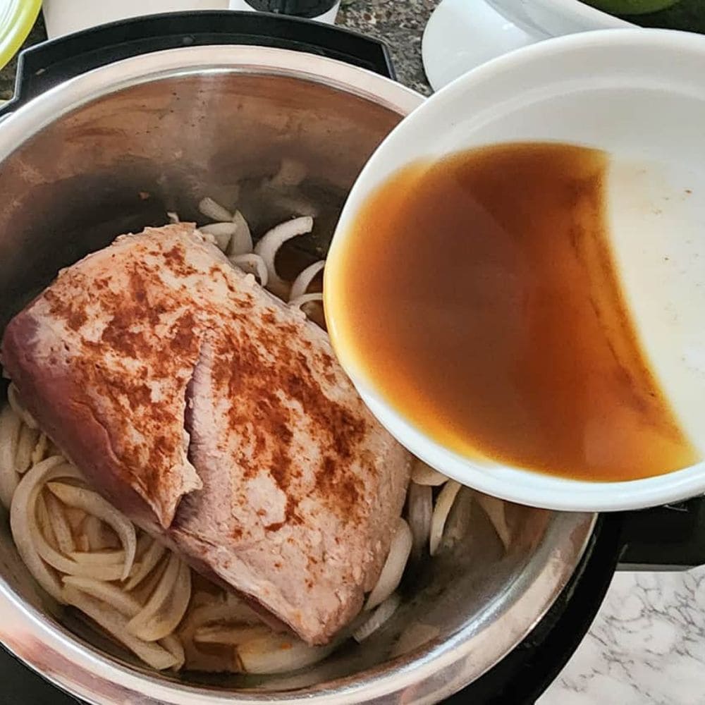 apple cider pork loin process step 3 cider pouring in to the Instant Pot with pork and onions