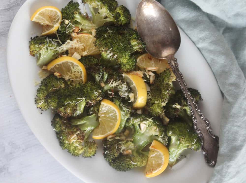 an overhead view of broccoli on a white platter with a spoon on the side