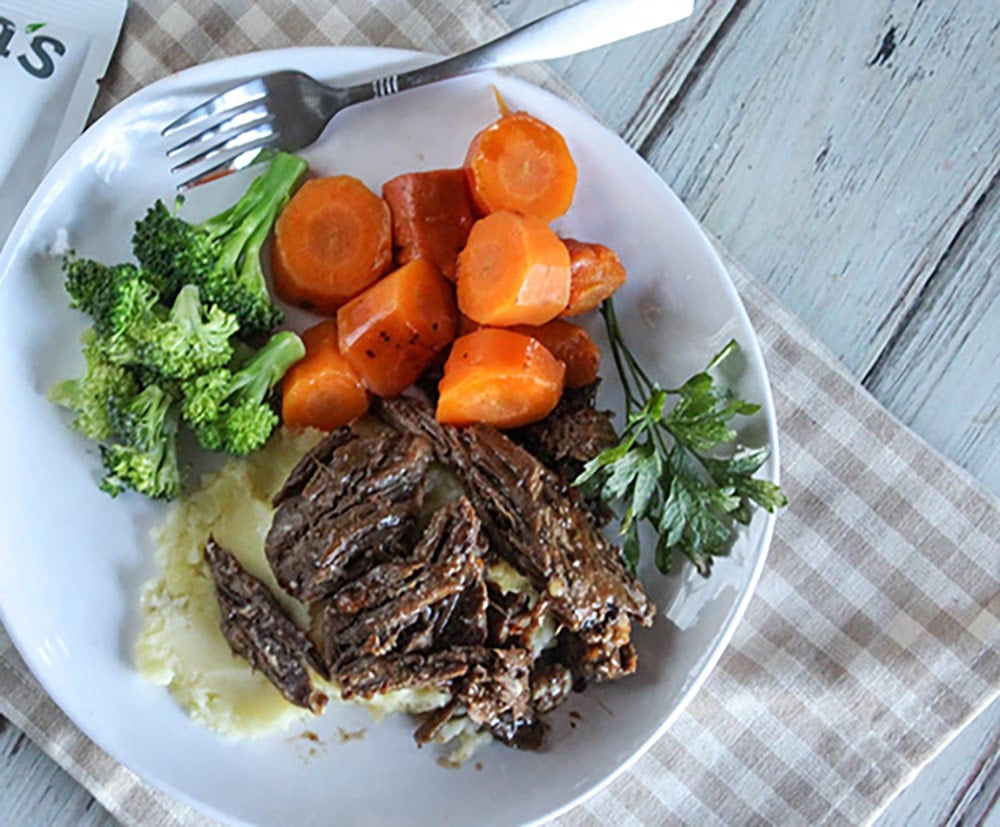 plated shredded beef pot roast covered with carrots and broccoli on the side on white plate and fork 