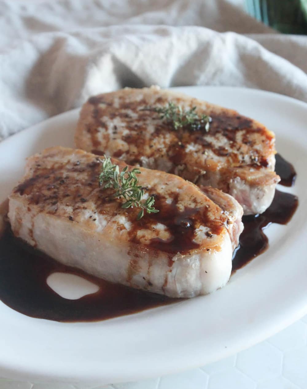 A picture of two boneless pork chops on a white place with balsamic vinegar sauce on top