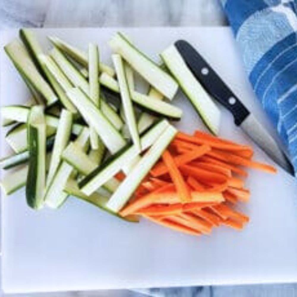 a picture of julienne sliced zucchini and carrots on a white cutting board with a knife