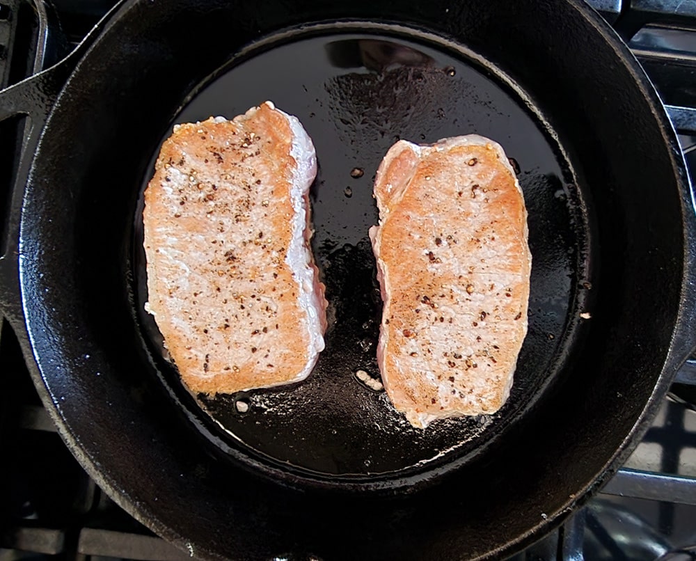 process 1 a picture of two boneless pork chops in a skillet cooking